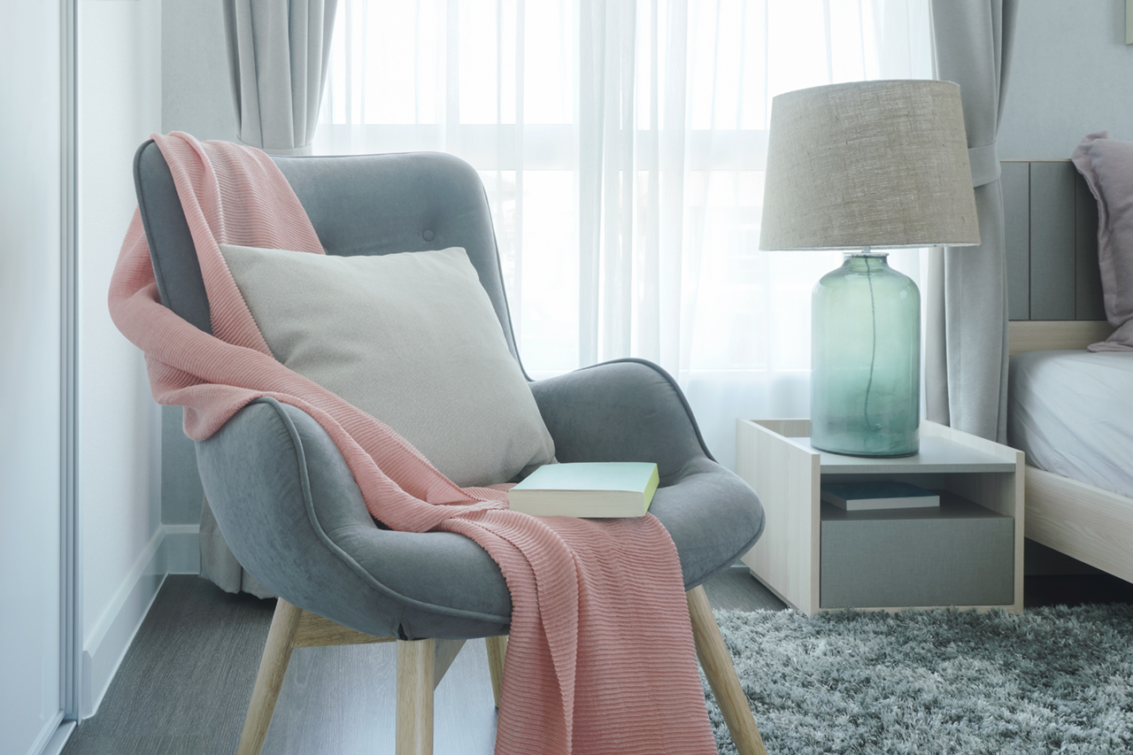 easy-armchair-with-pink-scarf-pillow-and-book-next-to-bed-in-the-bedroom